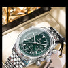 Reloj cronógrafo plateado con esfera verde y correa negra sobre una superficie clara.