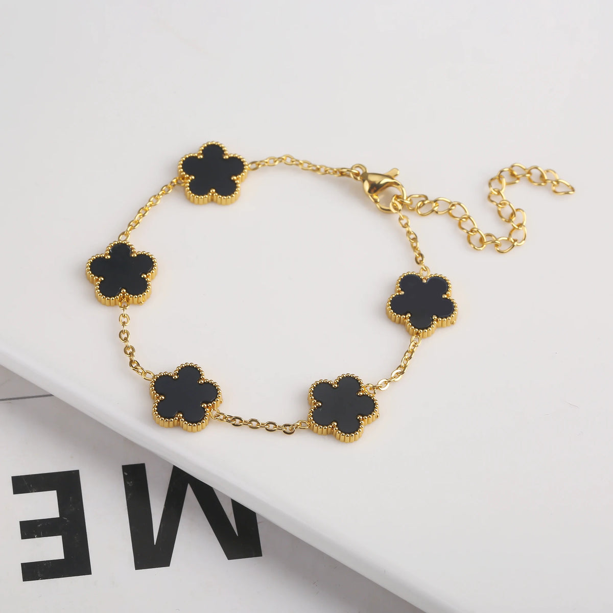 Pulsera de acero inoxidable chapada en oro con adornos de flores negras en una cadena dorada.