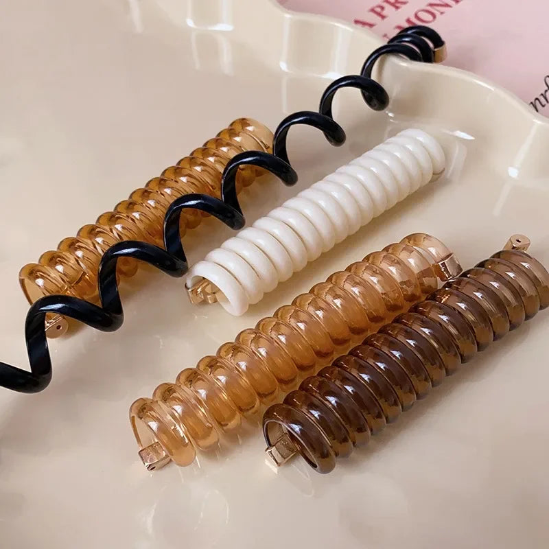 A set of rubber braided ponytail holders and scrunchies in black, gold, white, and amber colors.