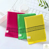 A set of three exfoliating bath washcloths in pink, green, and yellow with black stripes displayed on a white wire rack.