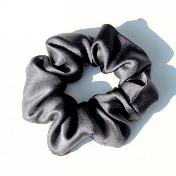 A black silk hair scrunchie with a gathered, ruched texture is shown against a white background.