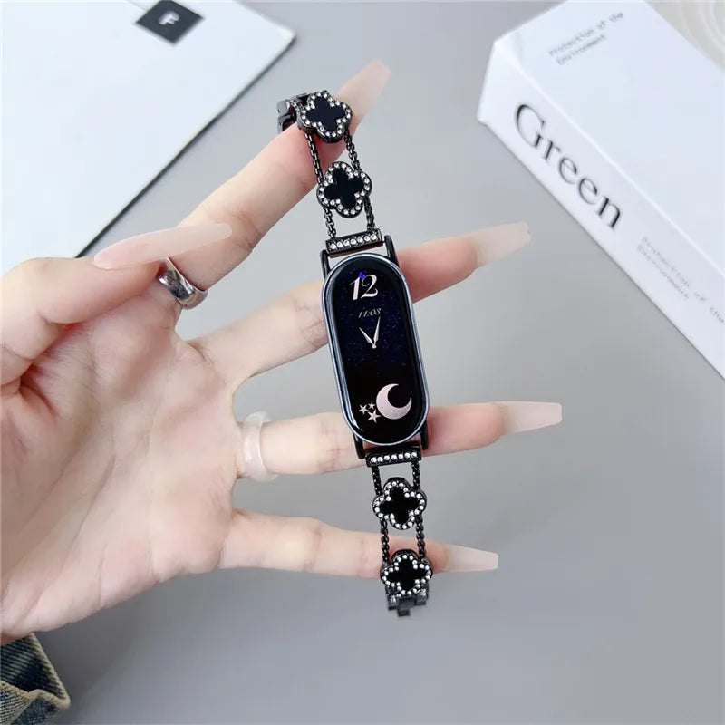 A hand is holding a black watch strap with a diamond four-leaf clover design, next to a green box.