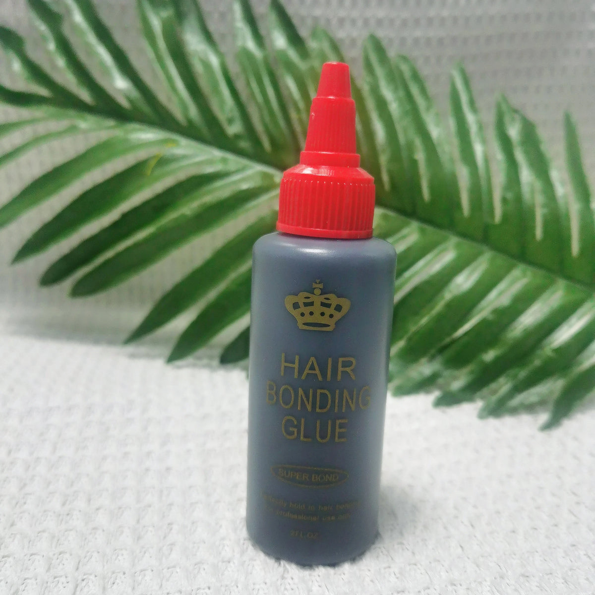 A bottle of professional hair bonding glue with a red cap and gray body is shown against a green palm leaf background.