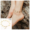 A close-up of a stainless steel snake chain anklet worn on a woman's ankle against a textured rock background.
