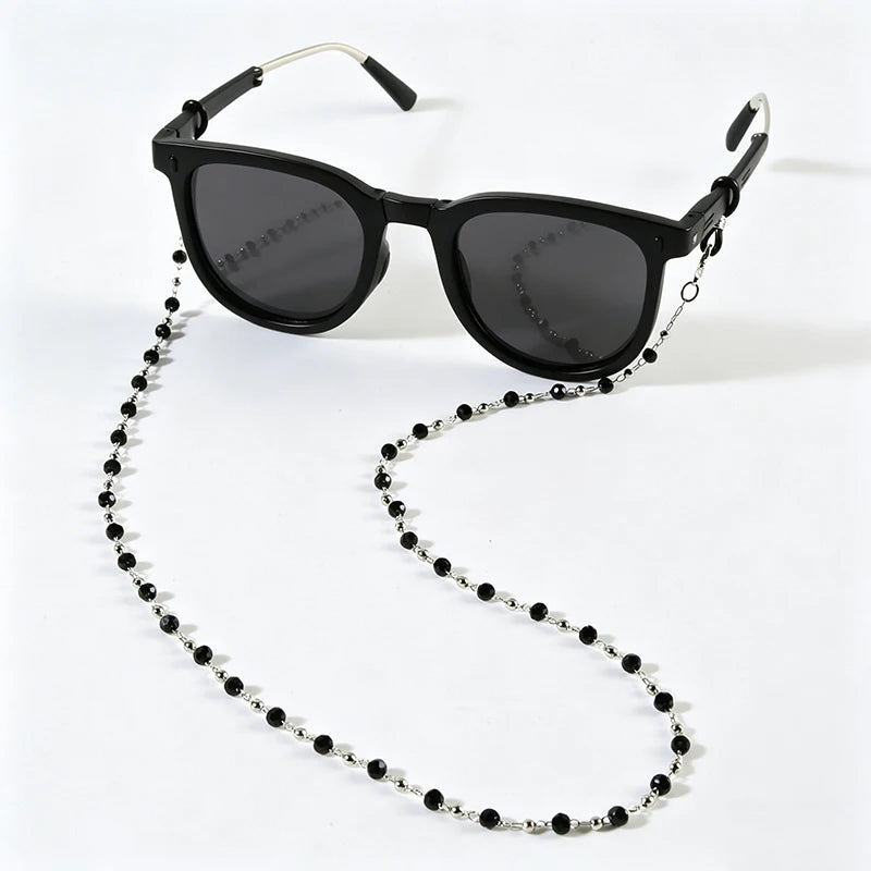 Black sunglasses with a chain of small black beads hanging from the arm.
