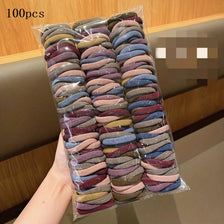 Un paquet de 100 élastiques colorés aux tons de violet, bleu et marron, tenu devant un fond en bois.