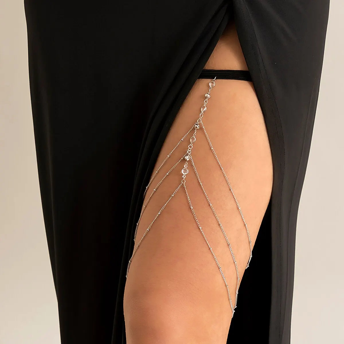 A close-up of a woman's leg showing delicate silver crystal body chain jewelry on the thigh.