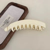A set of large, cream-colored banana hair clips resting on a wooden tray next to a white cloth.
