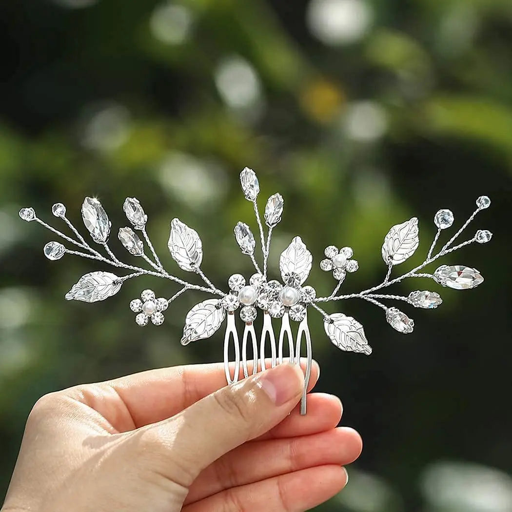 Une main tient une peigne pour cheveux de mariée en cristal ornée de feuilles et de fleurs délicates.