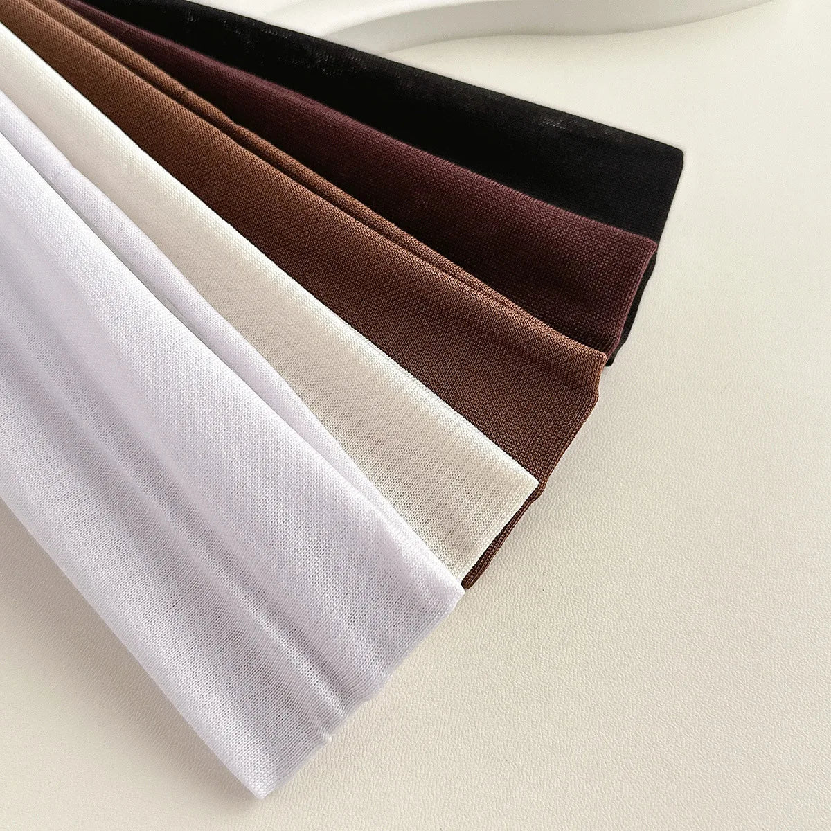 A stack of solid fabric headbands in shades of white, beige, brown, and black.