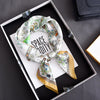 A floral print silk scarf tied in a knot, displayed in a black tray on a dark surface.