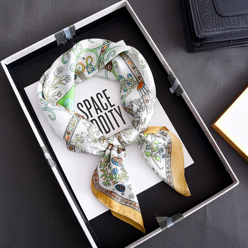 A floral print silk scarf tied in a knot, displayed in a black tray on a dark surface.