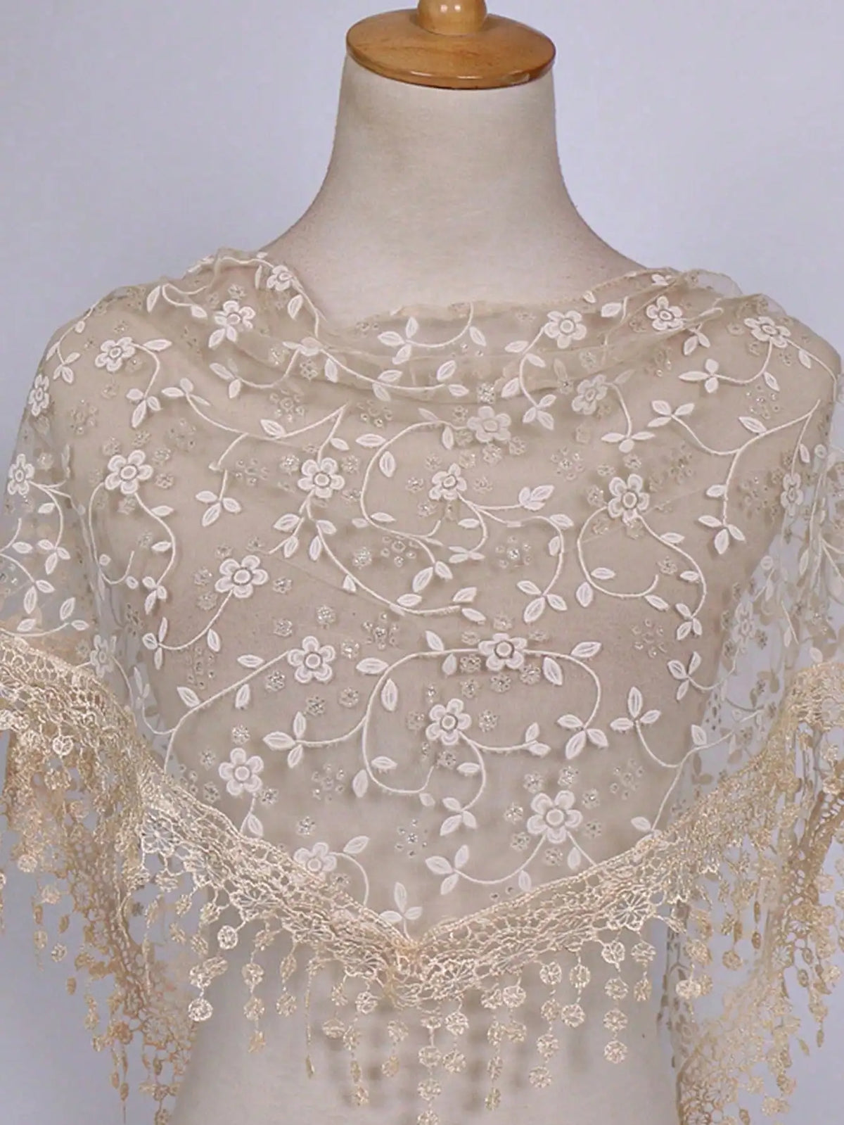 A sheer beige floral lace scarf draped over a mannequin neck.