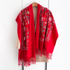 A vibrant red luxury floral scarf draped over a wooden hanger.