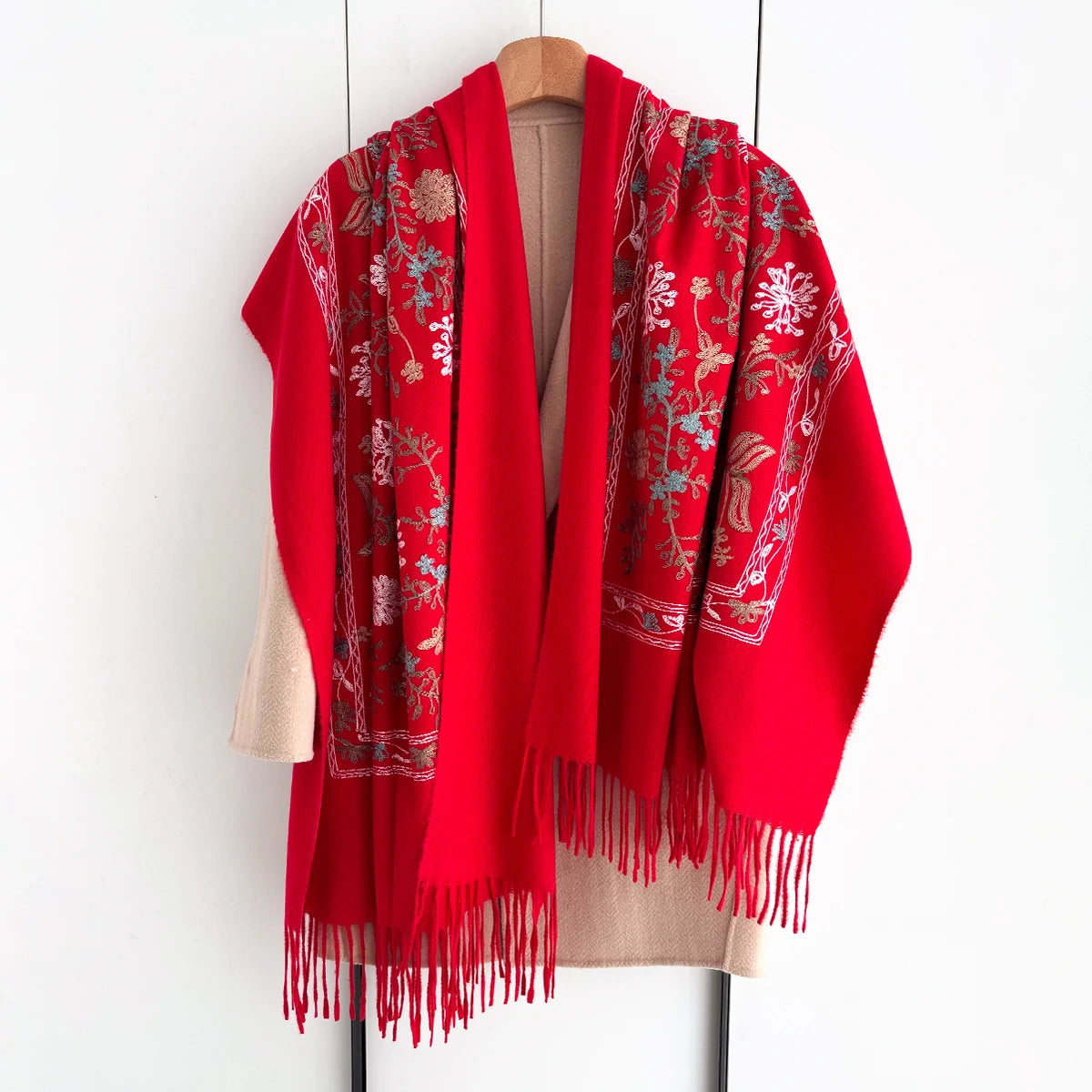 A vibrant red luxury floral scarf draped over a wooden hanger.