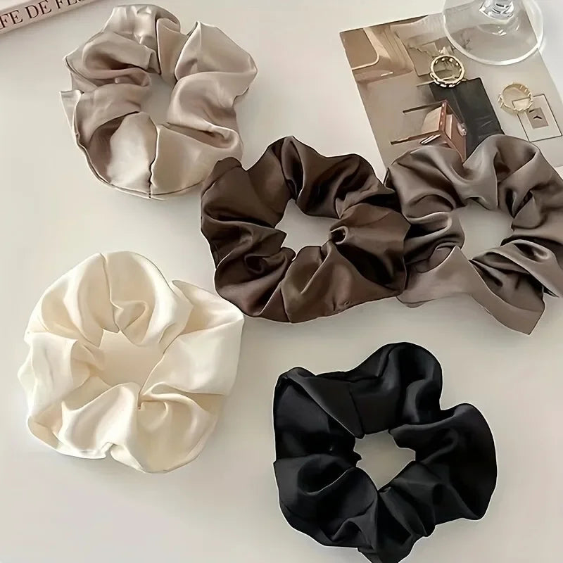 A collection of five elegant silk scrunchie hair ties in shades of beige, brown, and black.