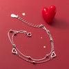 A sterling silver double heart charm bracelet displayed on a red background next to a red heart.