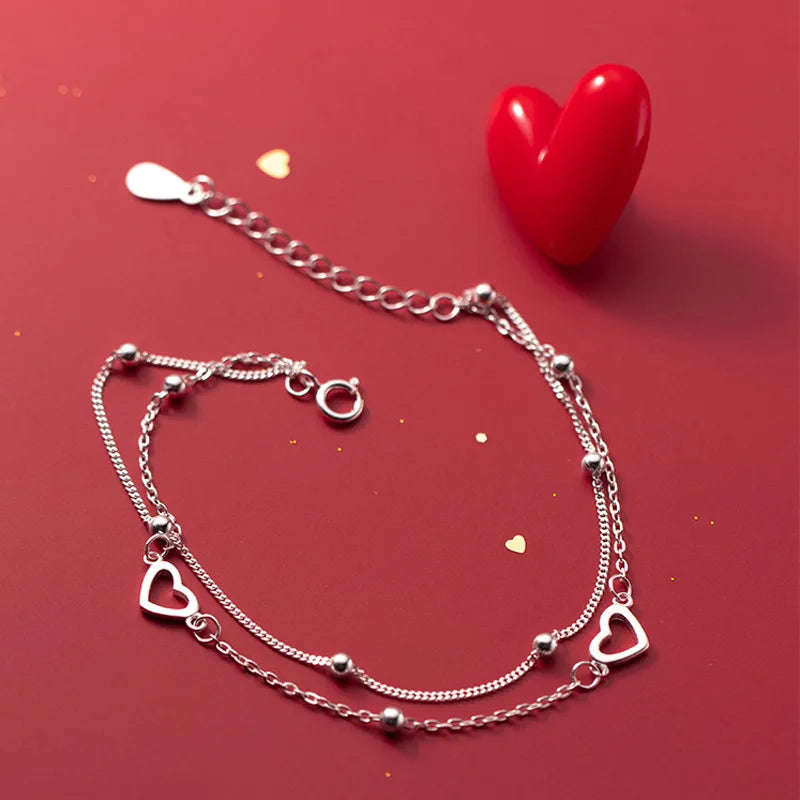A sterling silver double heart charm bracelet displayed on a red background next to a red heart.