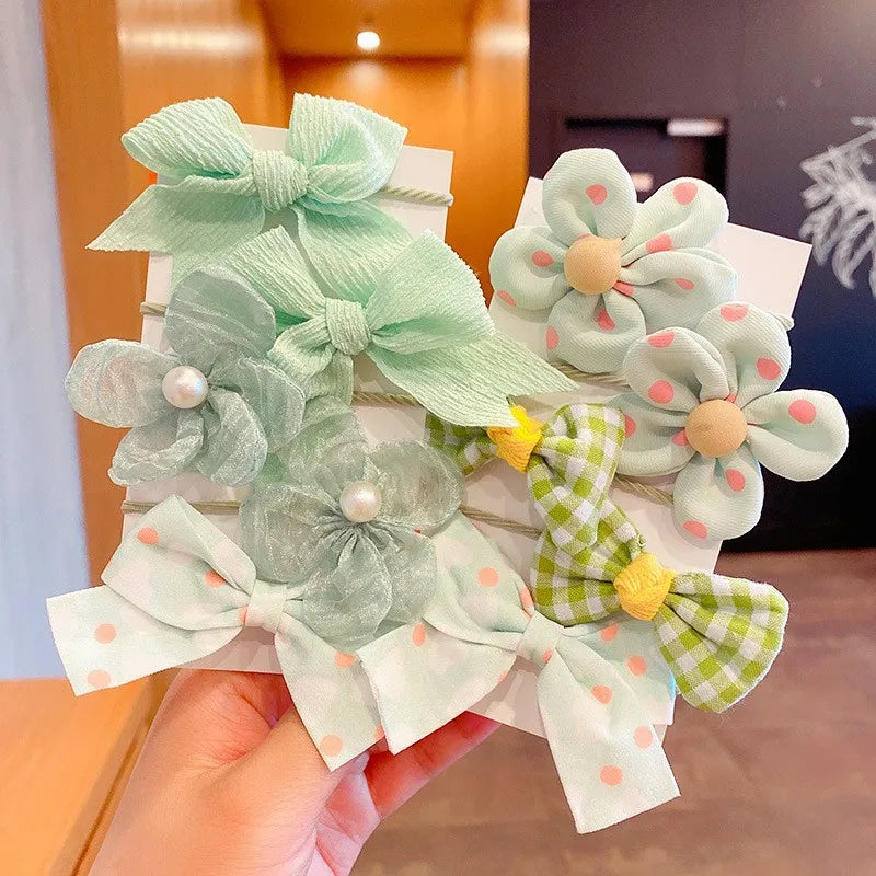 A hand holds a set of light green fabric flower bows and hair ties with pink polka dots and yellow accents.