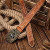 A brown PU leather floral engraved belt with a decorative buckle rests on a wooden surface next to thick rope.