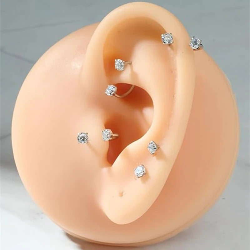 A set of small silver stud nose rings displayed on a light peach-colored ear model.