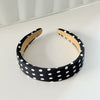 Black stretch hairband with white polka dots and tan lining lying on a white surface.