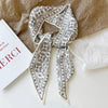 A silk satin hair and bag accessory featuring an intricate white and black patterned ribbon tied in a bow.