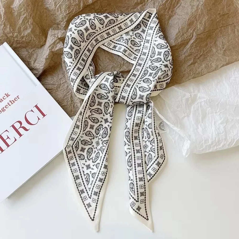 A silk satin hair and bag accessory featuring an intricate white and black patterned ribbon tied in a bow.