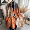 A draped orange and beige patterned cashmere scarf or shawl wrap displayed on a hanger.