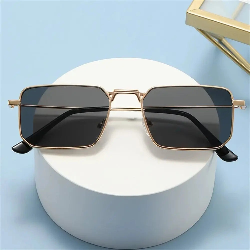 A pair of black sunglasses with a gold metal frame resting on a white surface.