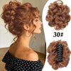 A woman shows off a voluminous curly messy bun hairstyle using a black claw clip hair accessory.