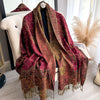 A richly colored bohemian paisley tassel shawl draped over a white chair.