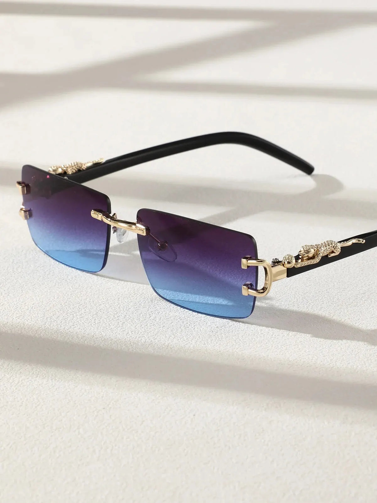A pair of trendy frameless rectangular sunglasses with purple-blue lenses and gold accents.