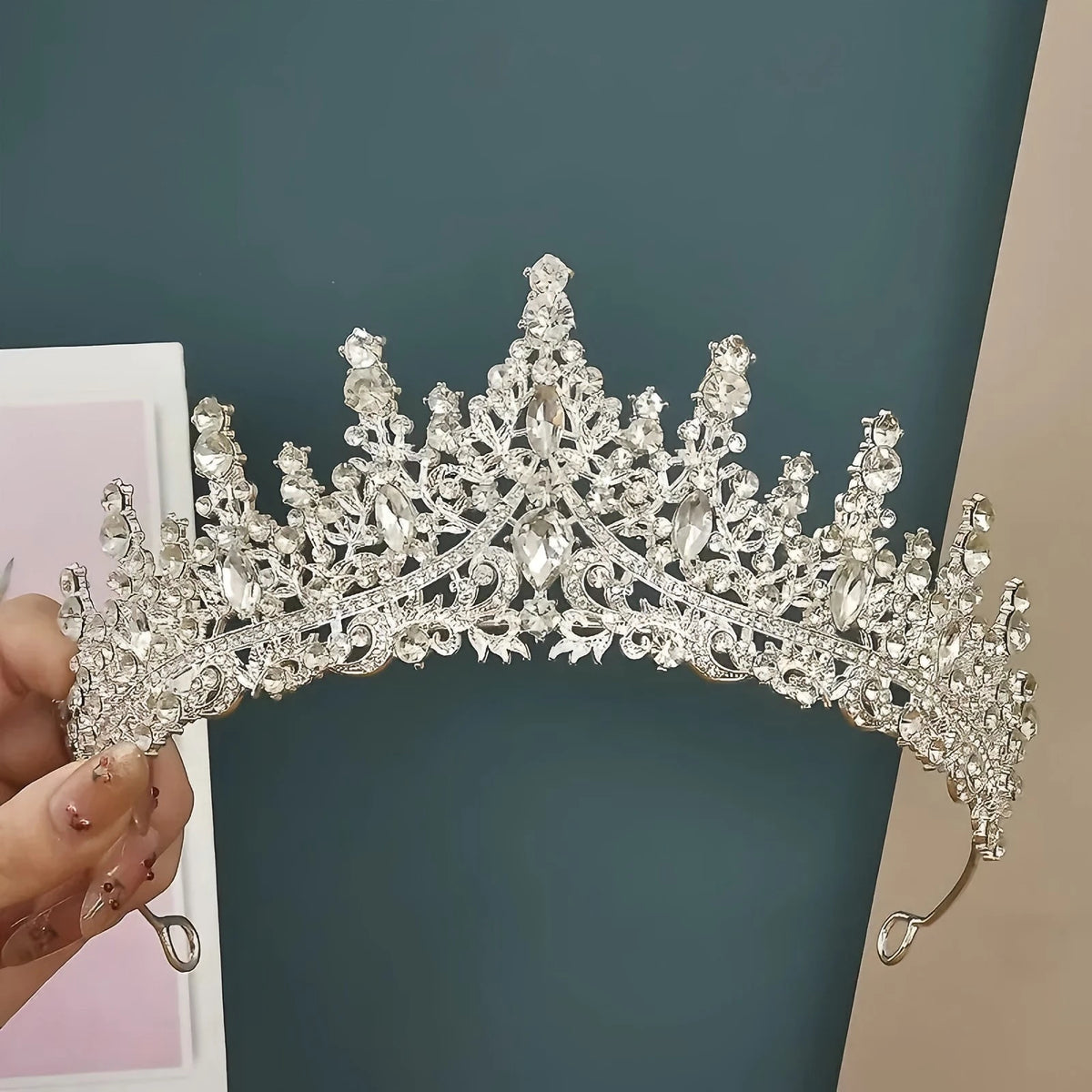 Primer plano de una elegante tiara de pedrería barroca bridal, sostenida contra un fondo verde azulado oscuro.