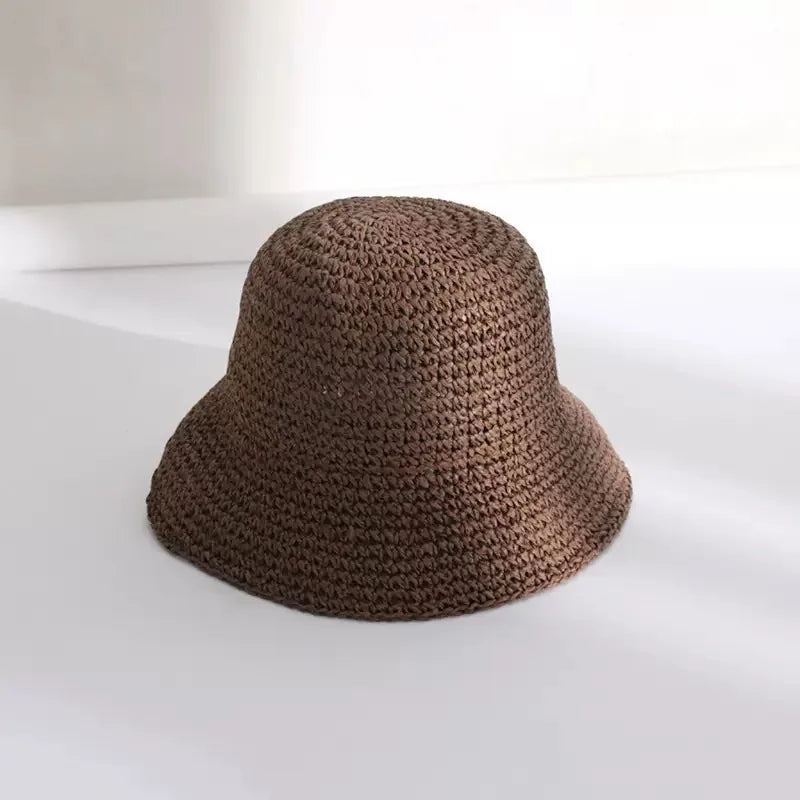 A close-up view of a brown hand-woven straw visor hat resting on a white surface.