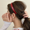 A woman is shown styling her hair with a red PU leather fashion headband.