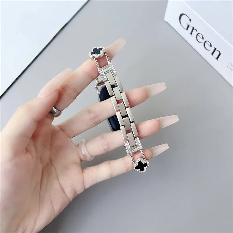 A hand is holding a silver diamond four-leaf clover watch strap for a Xiaomi Mi Band.