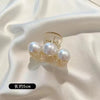 A pair of simulated pearl hair claws with gold-toned findings displayed on a white satin fabric.
