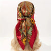 A red satin silk scarf with an ornate paisley pattern tied around a blonde wig.