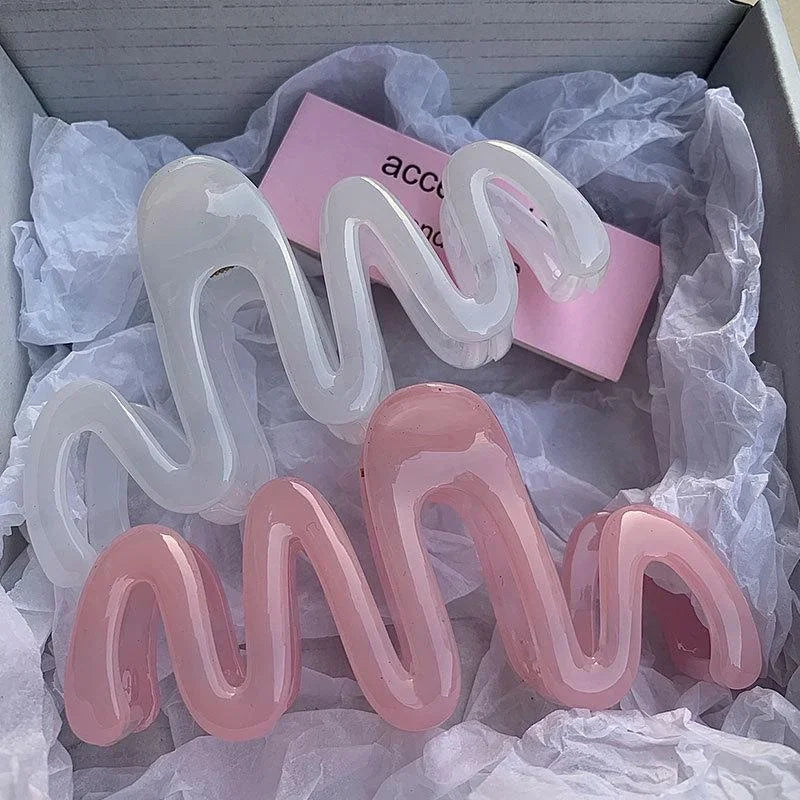 Una colección de pinzas para el cabello tipo ola de gelatina claras y rosas, exhibidas en una caja blanca forrada con papel d
