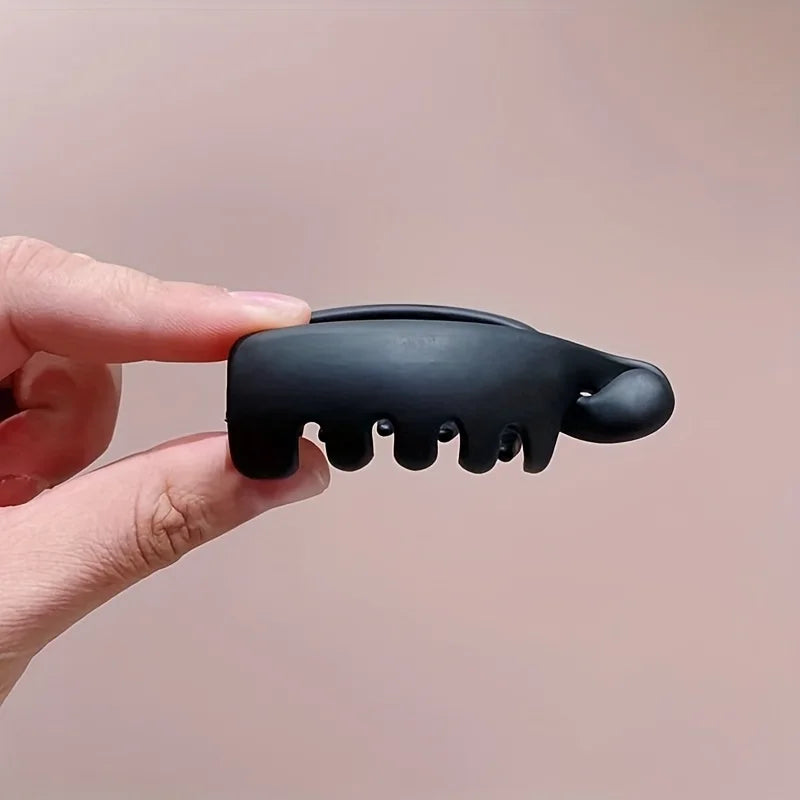 Una mano sostiene una pinza para el pelo de silicona negra con múltiples dientes pequeños, mostrando su textura y forma.