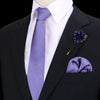Chaqueta negra con camisa blanca, corbata de seda púrpura, pañuelo de bolsillo de seda morado oscuro y broche floral.