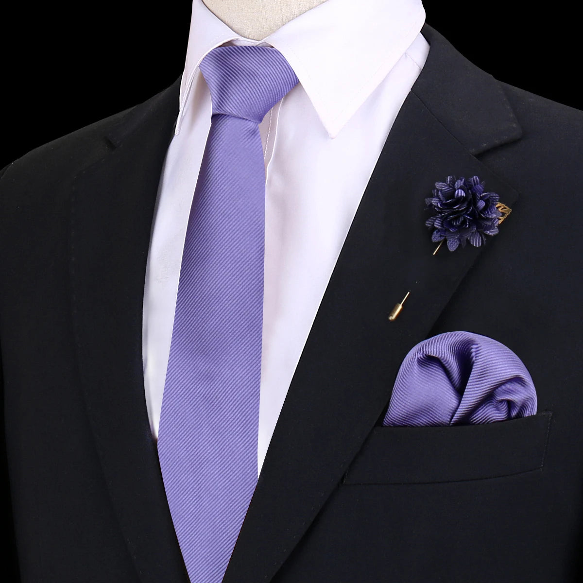 Chaqueta negra con camisa blanca, corbata de seda púrpura, pañuelo de bolsillo de seda morado oscuro y broche floral.