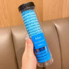 Una botella de plástico transparente llena de gomas para el pelo azules con rayas onduladas, sostenida por una mano.