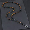 A rosary necklace featuring tiger eye and black agate beads with a hematite cross pendant on a dark gray background.
