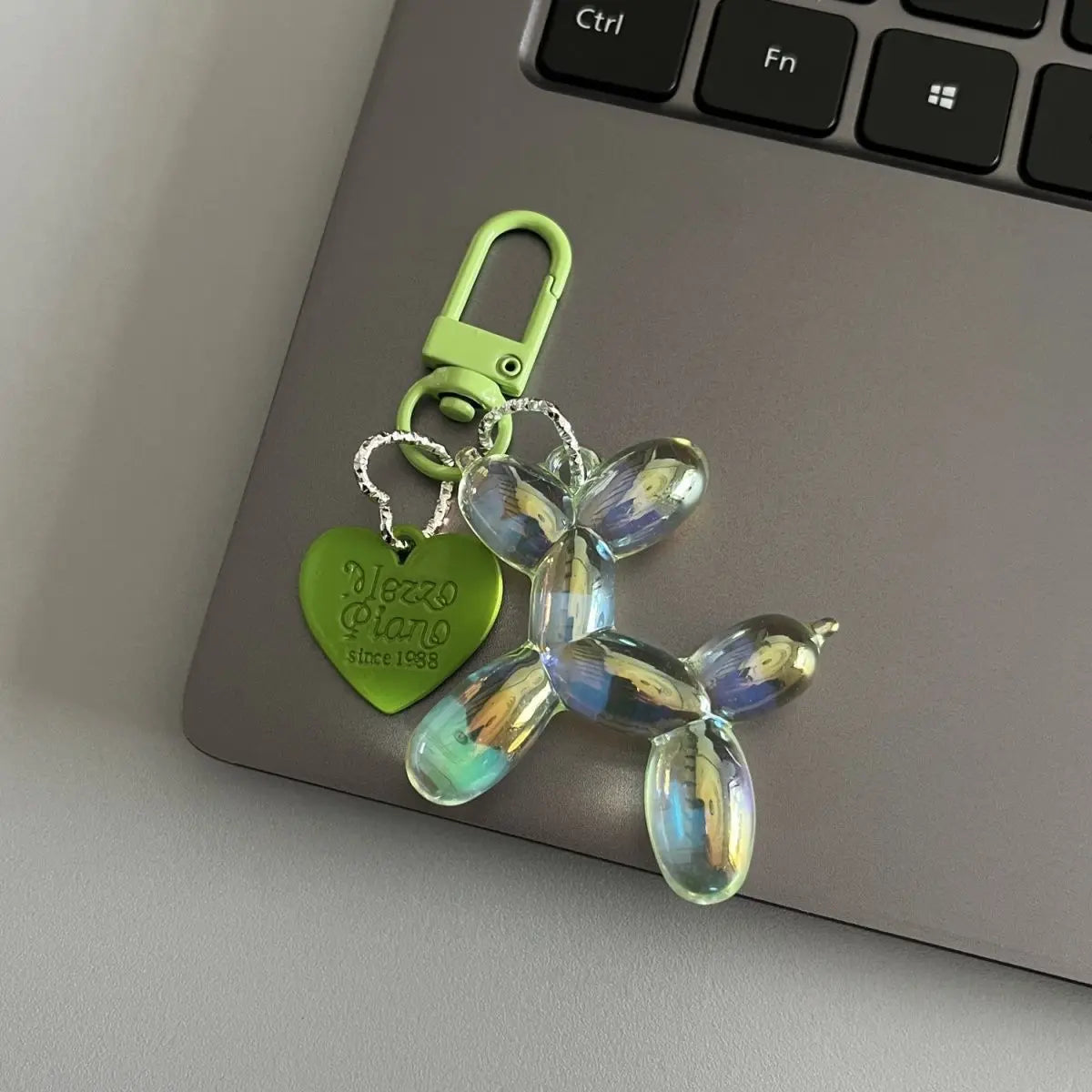 A clear resin animal dog keychain with a green metal clasp resting on a gray laptop.