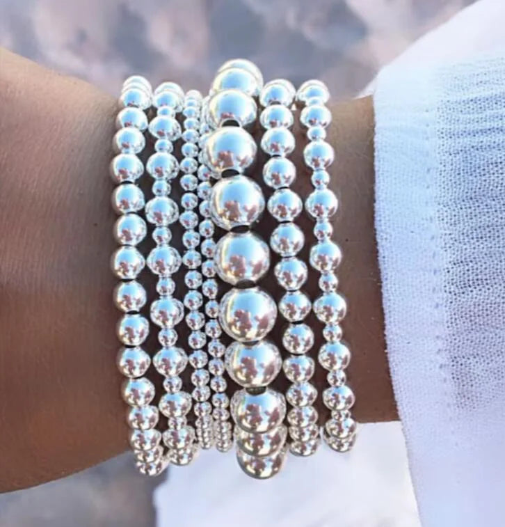 A stack of silver-toned round beads forming a bracelet set worn on a wrist.