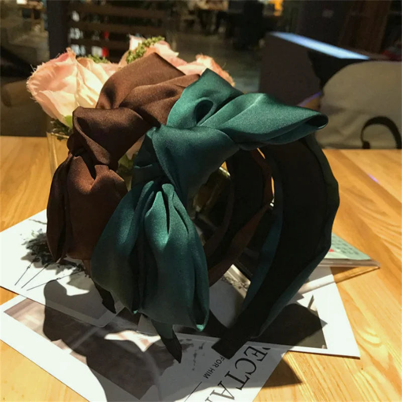 A dark green wide bow headband displayed on a wooden surface with floral accents.