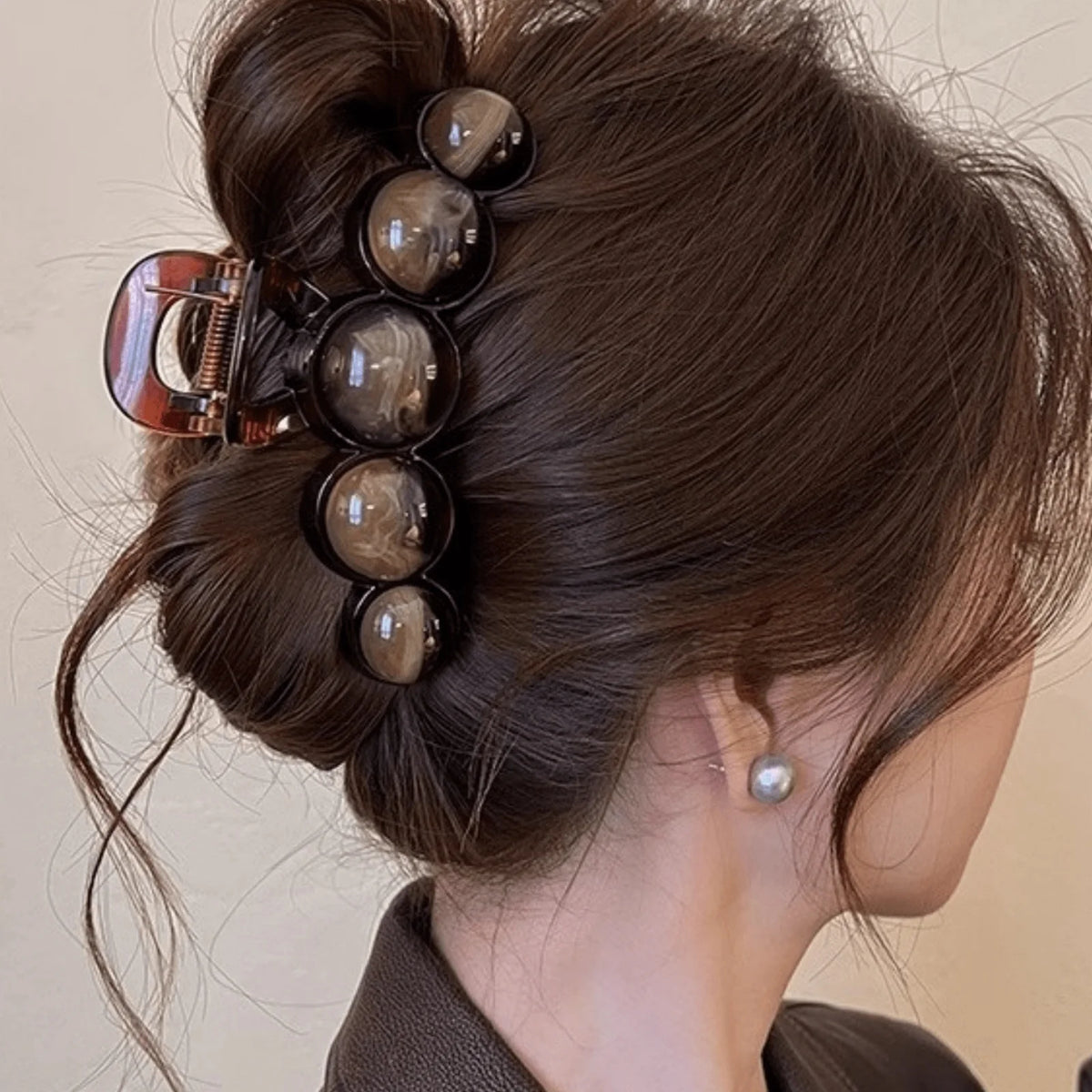 A dark brown hair styled in an elegant updo adorned with several glossy, spherical acrylic pearl hair claw clips.