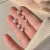 A hand holds three round, pearl-like stud earrings in gold-toned zinc alloy against a soft background.